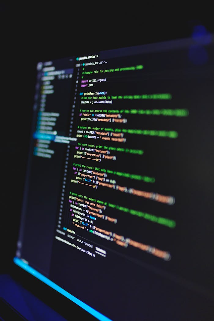 hero-img-01 Vertical shot of colorful programming code on a screen in a dark room, highlighting technology work.